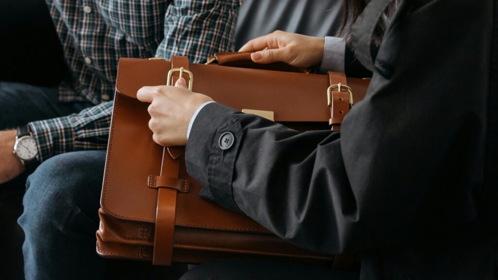 A man seated on a couch holds a brown briefcase