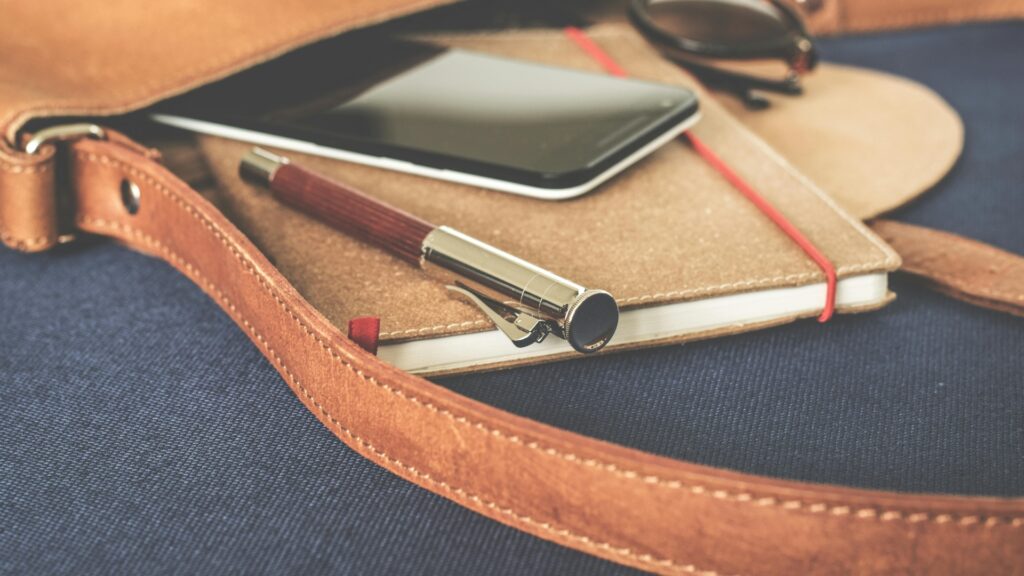Leather bag with a pen, notebook, phone, and glasses