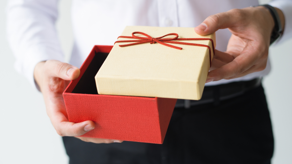 A man stands holding a colorful red and yellow gift box.