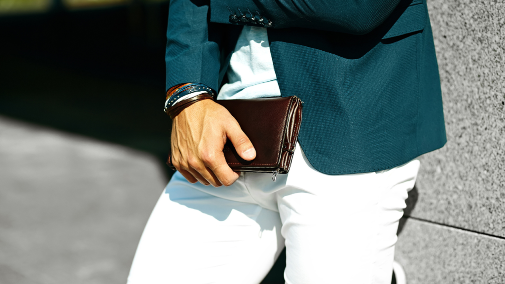 A man in a blue blazer and white pants is holding a wallet in his right hand.