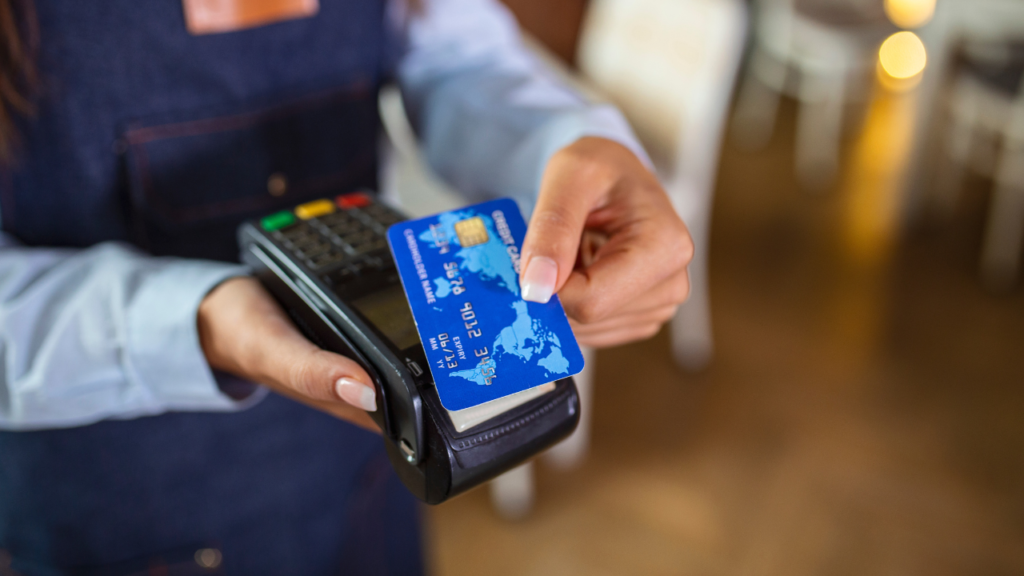 A woman is using a credit card while standing by a cash register.