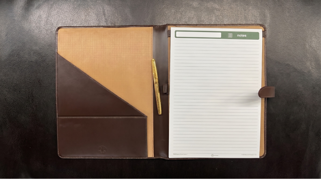 An open leather meeting folder featuring a lined notepad on the right and a pen on the left.