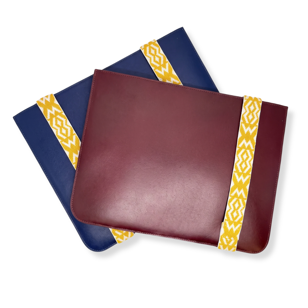 Stacked burgundy and navy blue 13-inch leather laptop sleeves by The Leather Collection, each secured with a yellow and white geometric patterned elastic band.